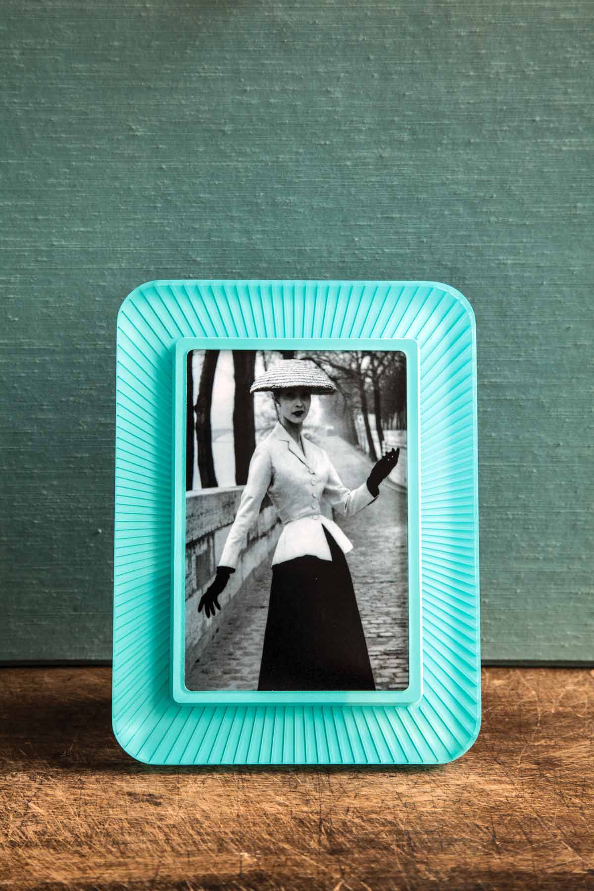 Ray Island Prisma frame with rounded edges and ridges, in a beautiful turquoise blue, framing a black and white image of a woman on a clean wooden surface with a teal backdrop