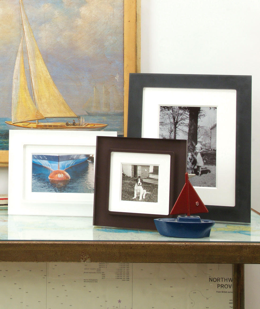 Grouping of chocolate brown, white and black frames on a glass desk with sailing decor and family photos